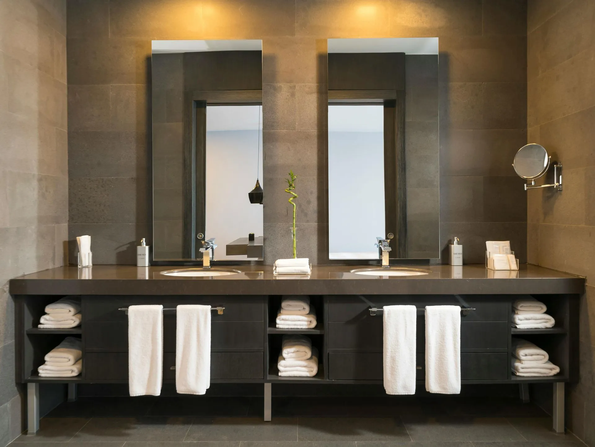 Bathroom with dual sinks, large mirrors, dark grey countertop and cabinetry, and white towels.