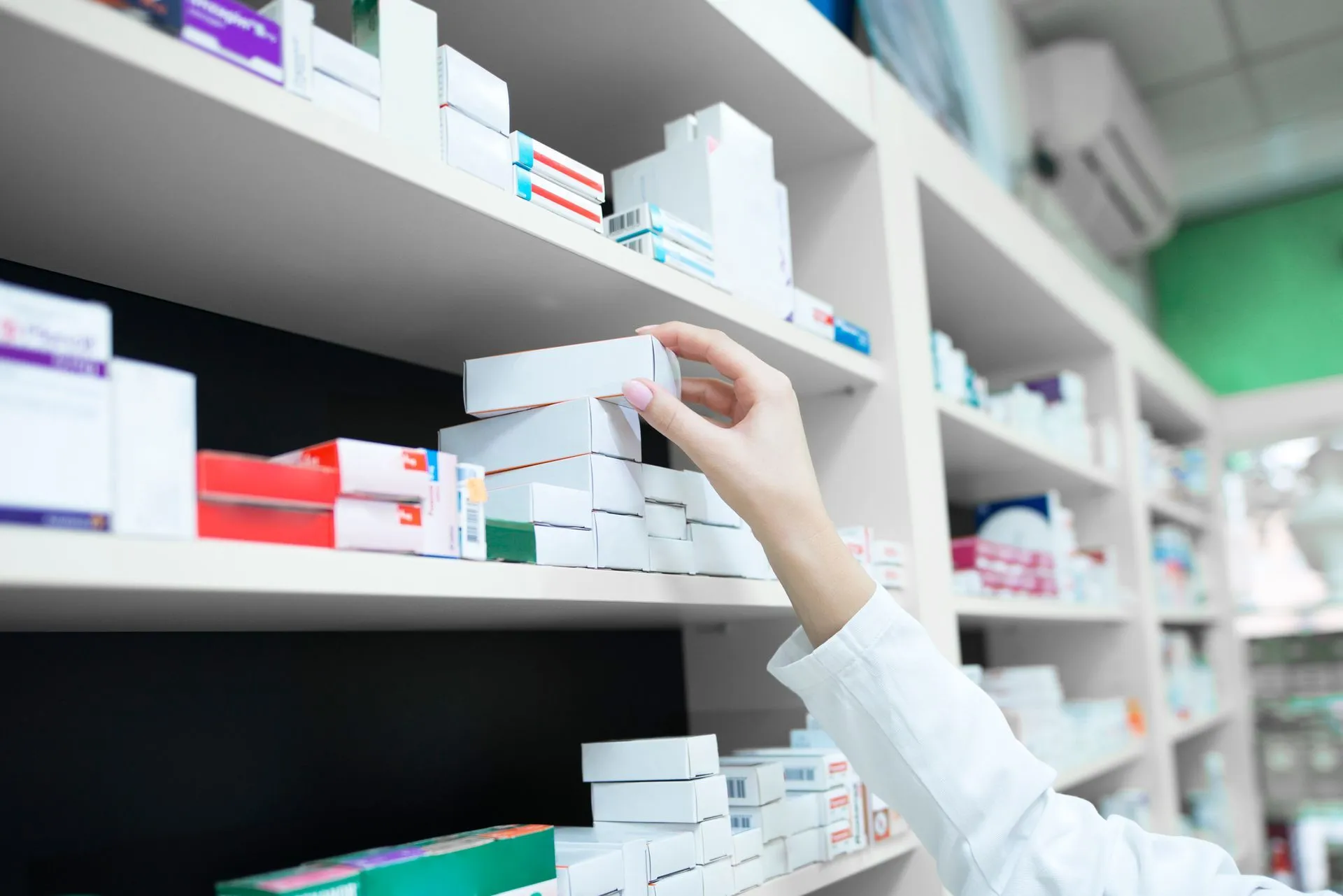 Pharmacist's hand taking a box of prescription medicine from a pharmacy shelf