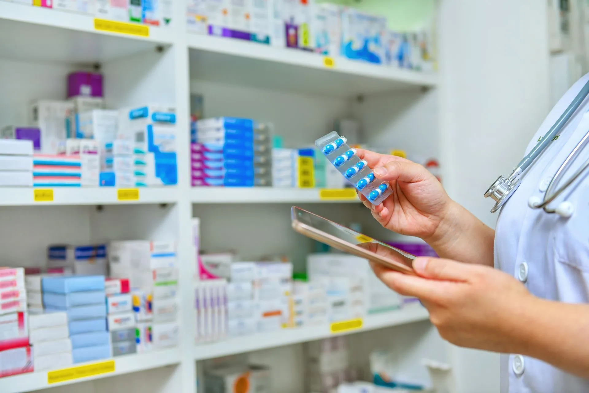 Pharmacist examining medication from shelf, holding tablet blister pack, looking at a tablet.