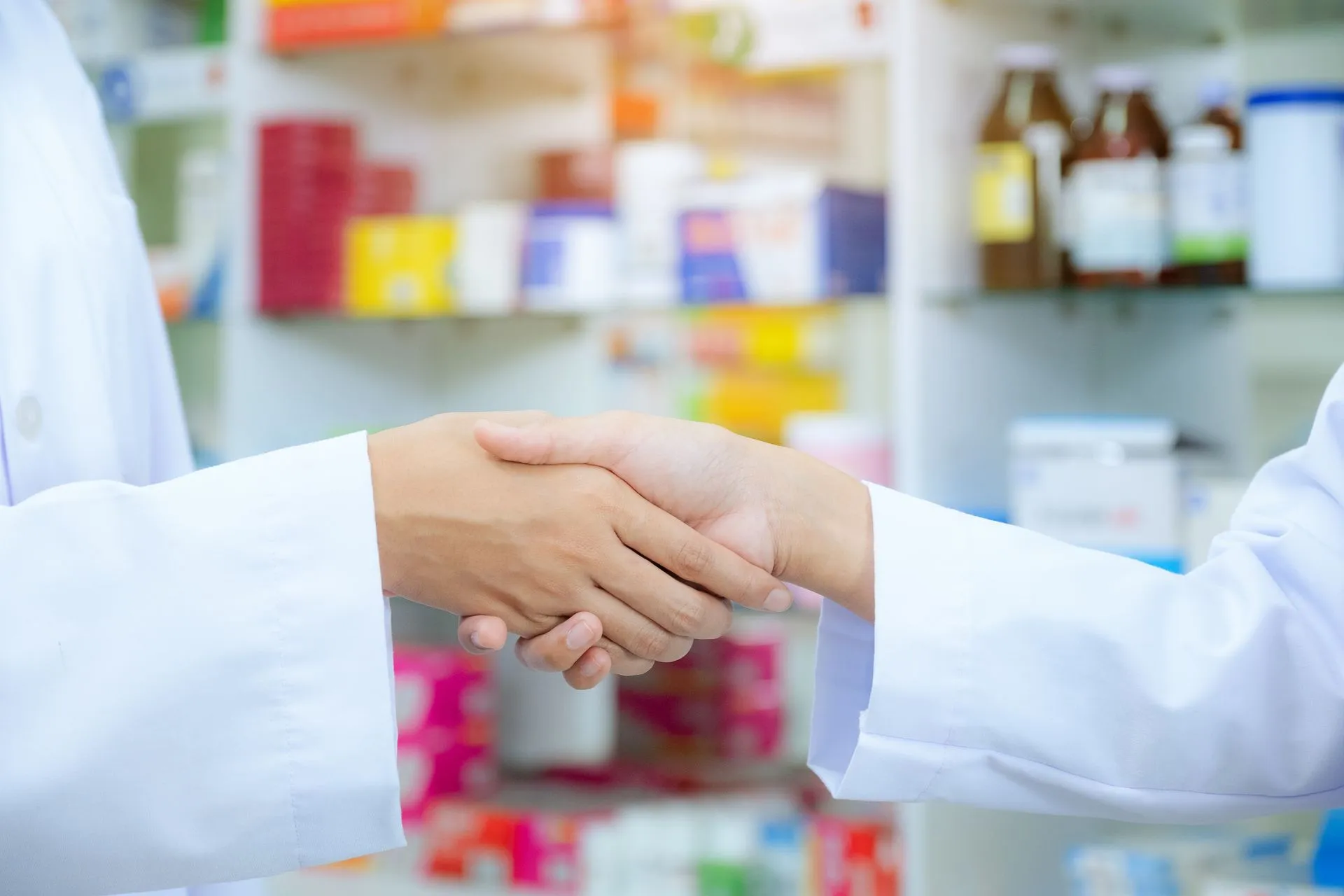 Two pharmacists in white coats shaking hands inside a pharmacy