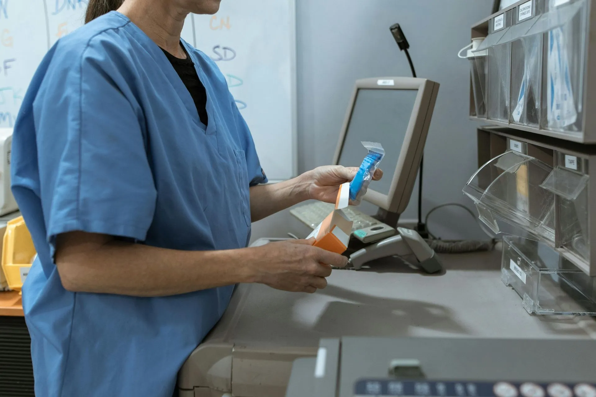 Person in blue scrubs working at a pharmacy counter, scanning medication bottles.